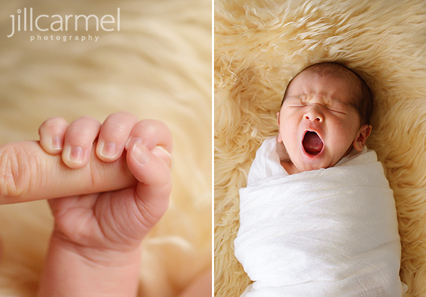 Newborn baby yawning swaddled in a white blanket laying on top of a sheepskin rug and newborn fist grasping mom's finger