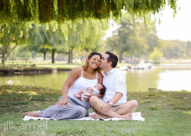 Mom and dad with newborn baby sitting in the shade of a willow tree in Sacramento