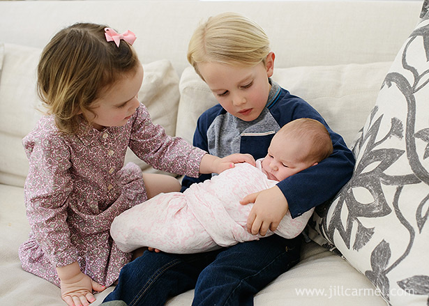 big brother holds his baby sister while the kids cuddle on the sofa during this newborn session in los angeles | Jill Carmel