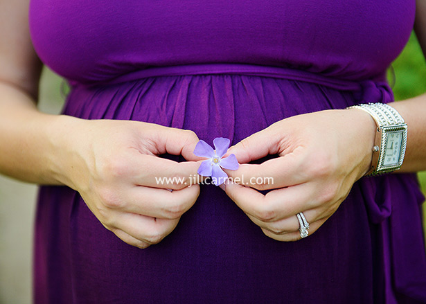 holding a small purple flower in front of her pregnant belly