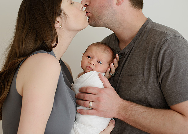 mom and dad kissing over newborn son in sacramento studio