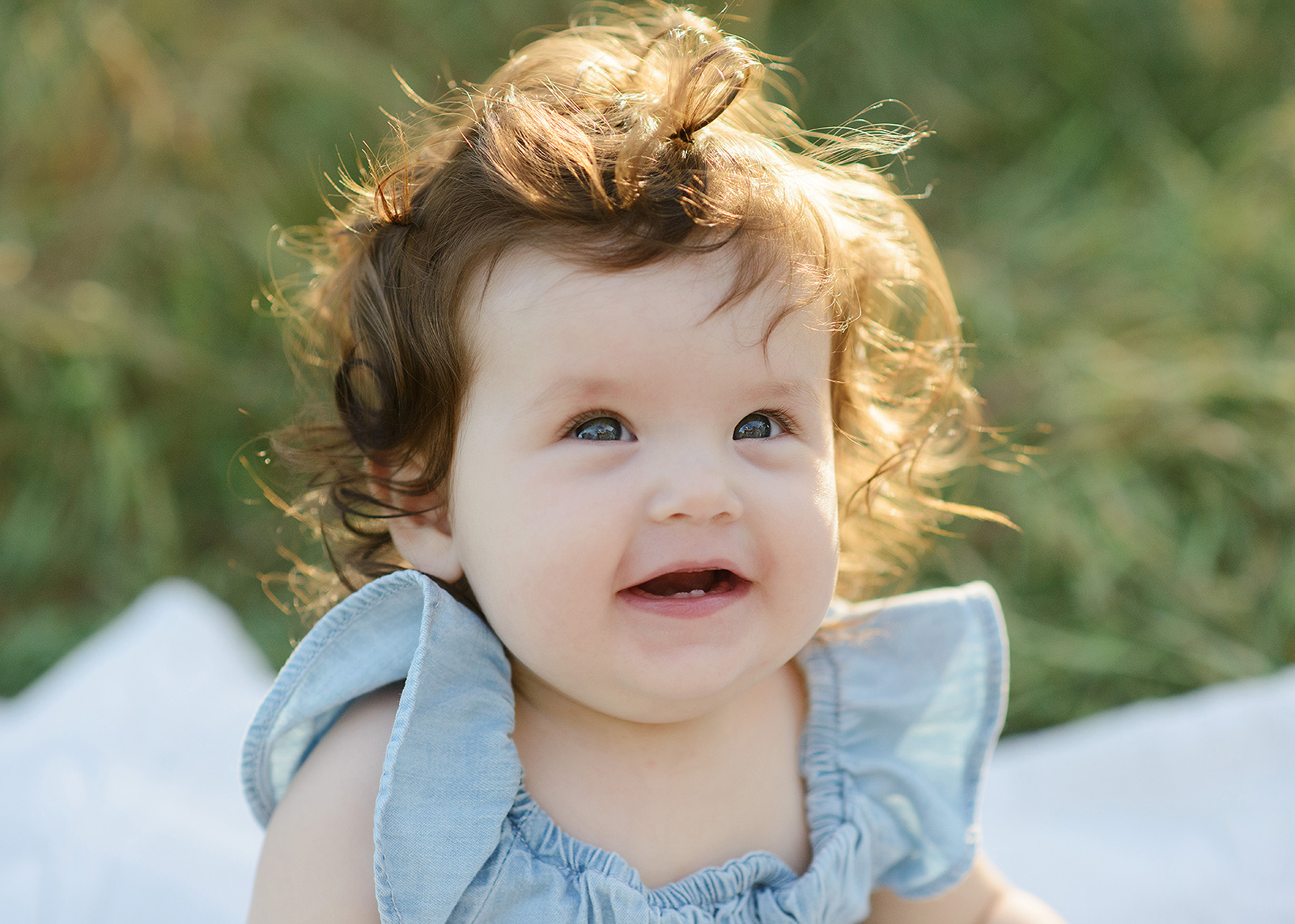 Smiling baby with curly hair in the sun and chambray dress