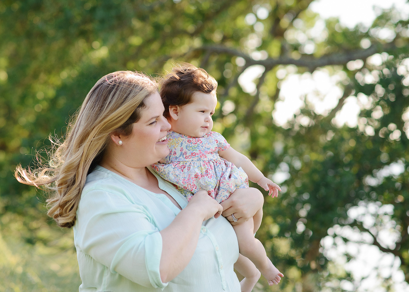 Mom holding baby with wind-blown hair against the trees with spring outfits in folsom