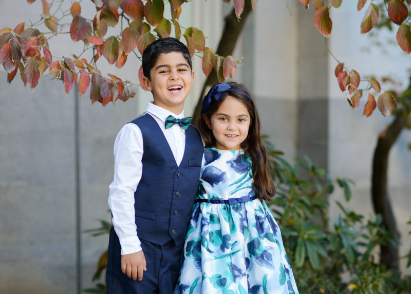 Brother and sister wearing blue smiling in front of trees