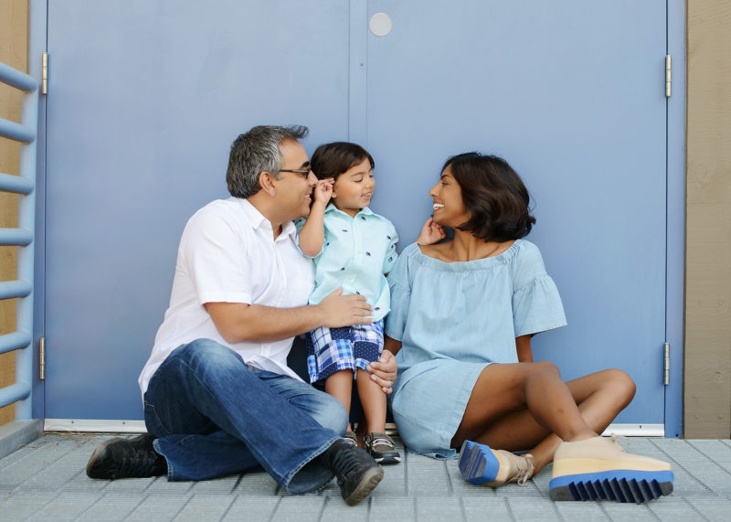 Dad, mom and son smile at each other in front of baby blue door at Folsom Powerhouse