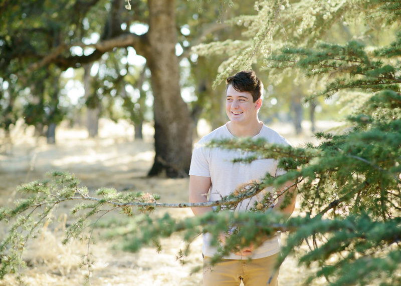 Teenage male smiling in between trees in Folsom