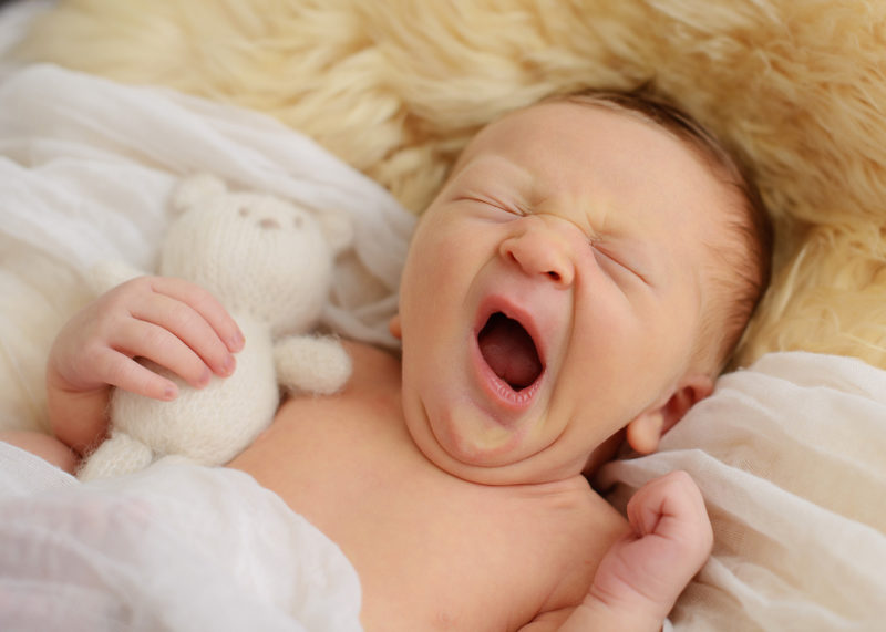 Newborn baby boy yawning on fur throw