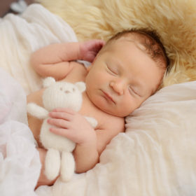 Sleeping newborn baby boy cuddling with stuffed bear toy
