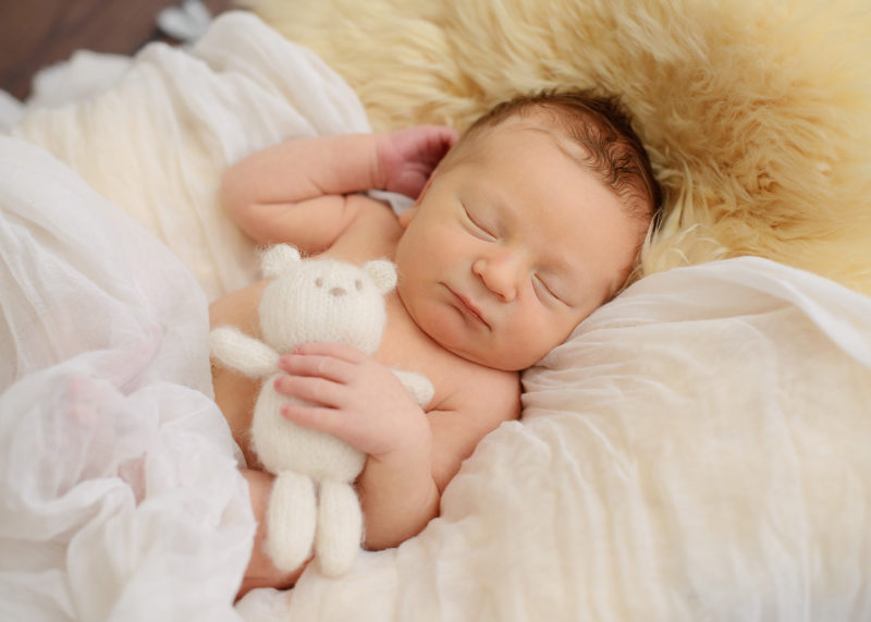 Sleeping newborn baby boy cuddling with stuffed bear toy