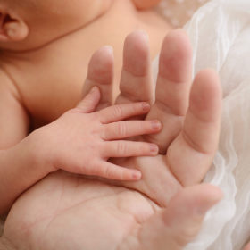 Tiny baby hands on moms hand on muslin sheet