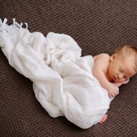 Newborn baby boy dreaming in loose muslin swaddle and brown background