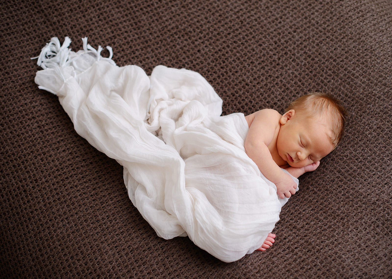 Newborn baby boy dreaming in loose muslin swaddle and brown background