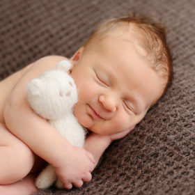 Newborn baby boy cuddling with stuffed white bear while sleeping