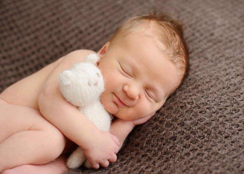 Newborn baby boy cuddling with stuffed white bear while sleeping