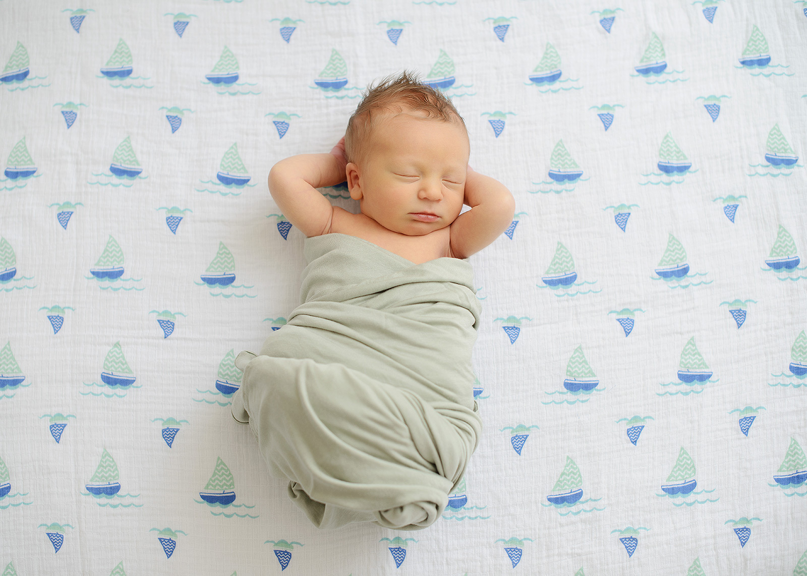 Newborn baby boy chilling with arms up on sailboat pattern sheet