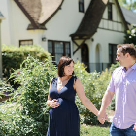 Pregnant couple holding hands and smiling in front of their home