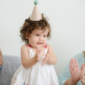 Baby Girl’s First Birthday in Party Hat and Parents Clapping