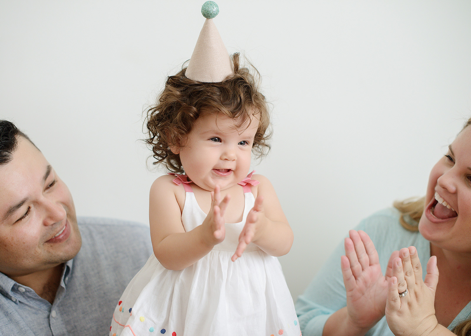 Baby Girl's First Birthday in Party Hat and Parents Clapping