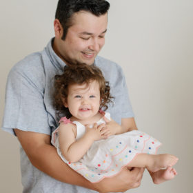 Dad Holding Baby Girl Who is Smiling Against White Background