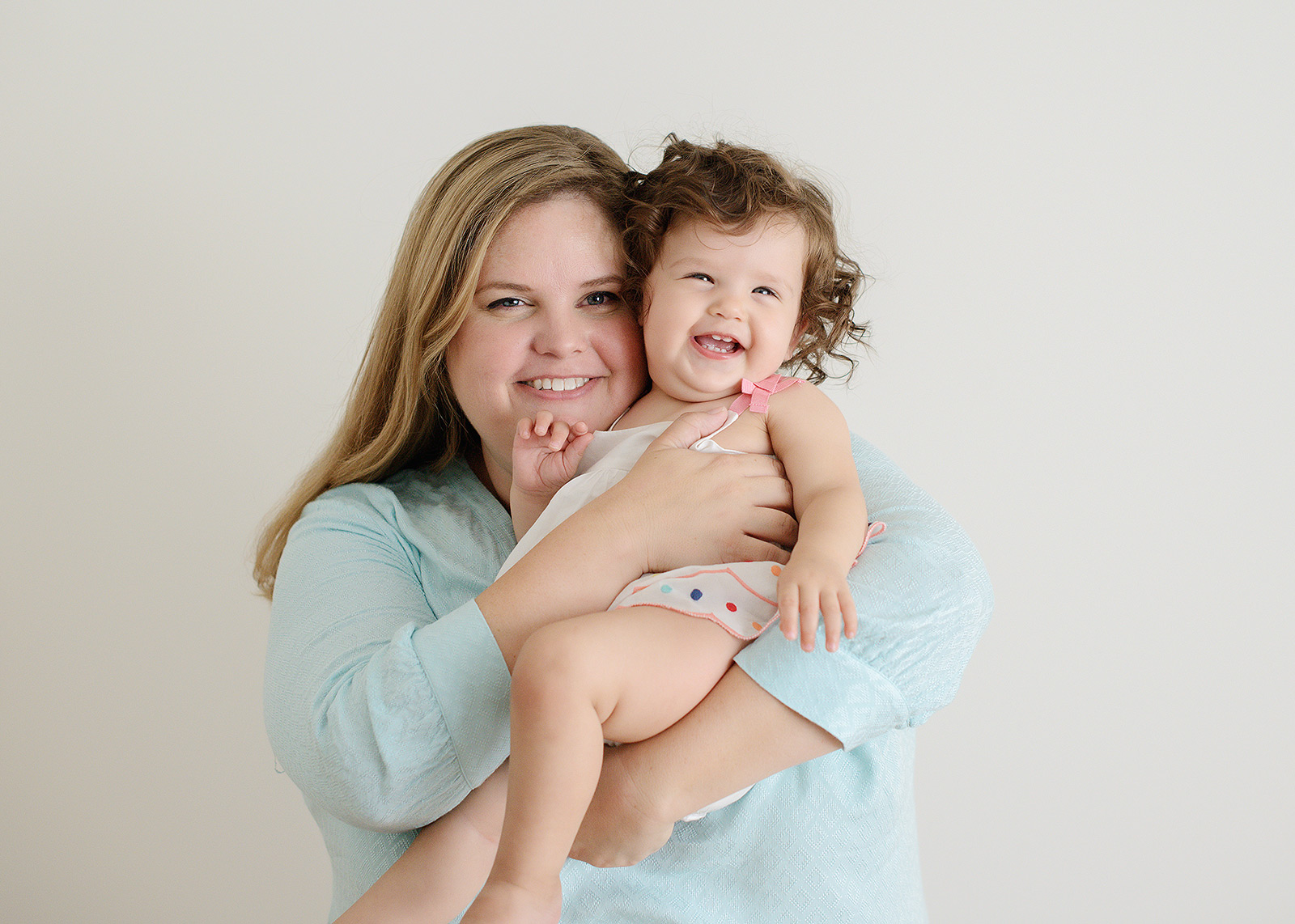 Mom Holds Baby Girl While Laughing Against White Background