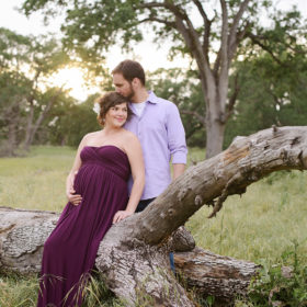 Pregnant couple sitting on fallen tree log outdoors in Folsom