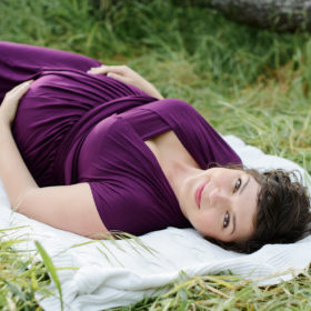 Maternity photos lying down in grass wearing purple dress in Folsom