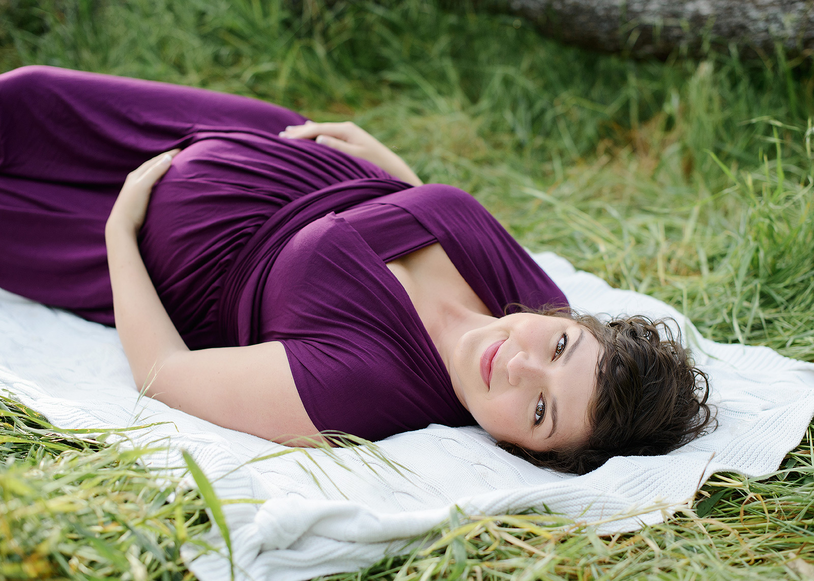 Maternity photos lying down in grass wearing purple dress in Folsom