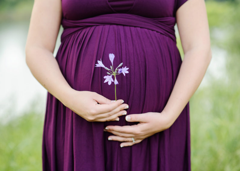 Pregnant woman wearing purple dress holding purple wildflower in Folsom