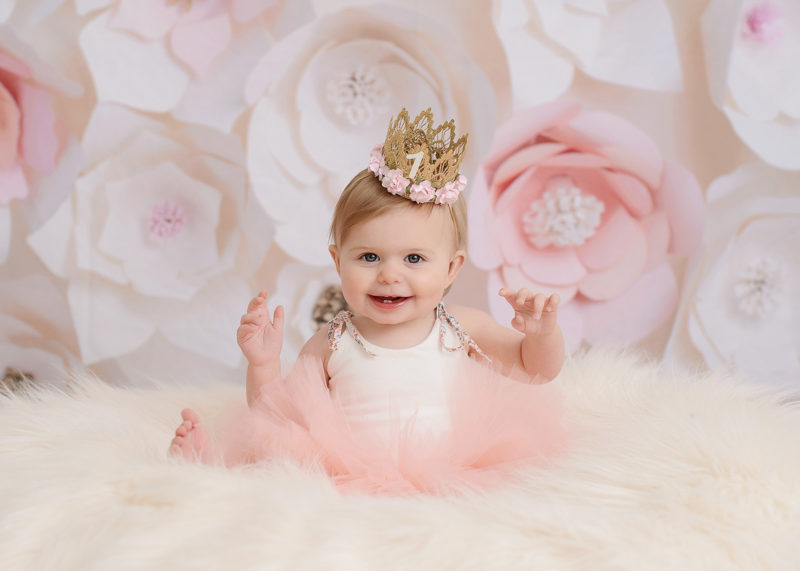 One year old girl wearing pink tutu and crown against floral backdrop