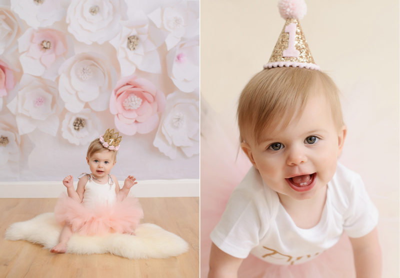 One year old baby girl in pink tutu smiling against paper flowers