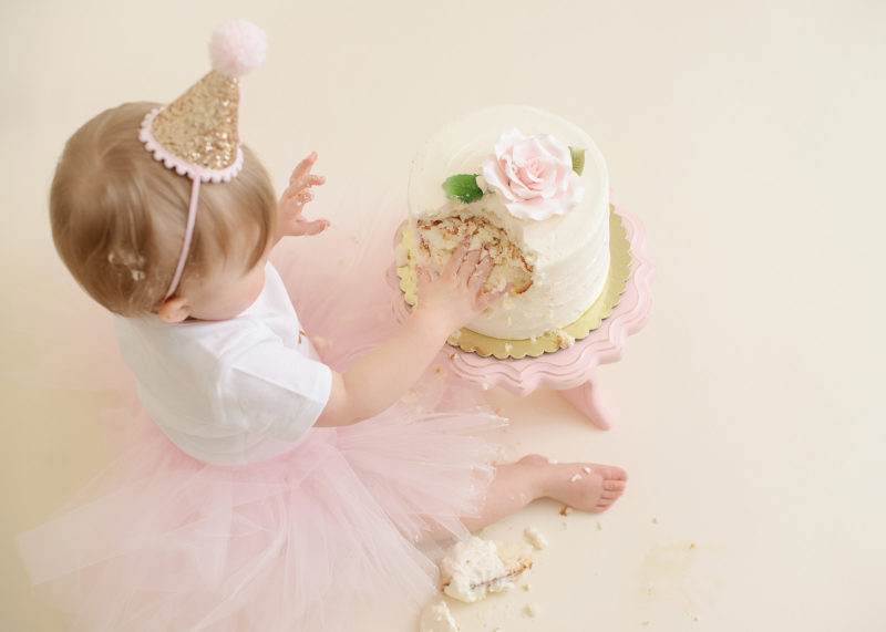 Baby girl in pink tutu smashing cake from top