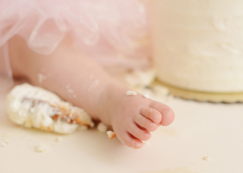 Baby girl wearing tutu with frosting on feet from cake smash