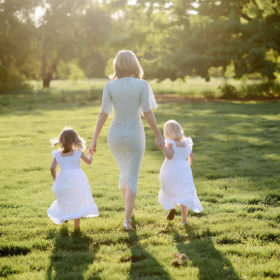 Mom and daughters walking towards the woods in grass during sunset in Sacramento