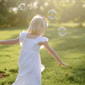 Daughter in white dress chasing after bubbles during Spring sunset