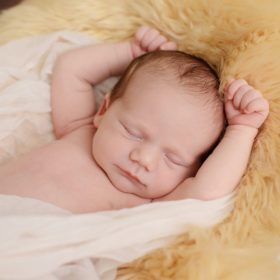 Newborn baby girl sleeping with arms up in muslin cloth and fur throw