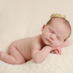 Newborn baby girl wearing crown on beige blanket