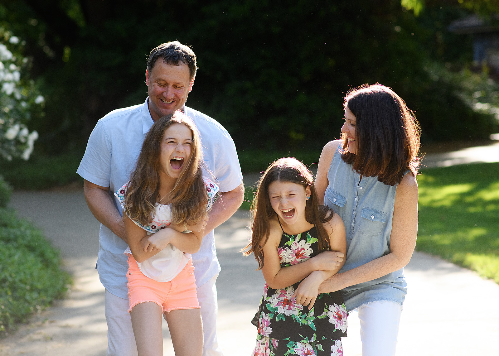 Mom and dad hugging daughters and laughing outdoors in Sacramento
