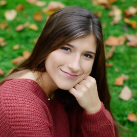Senior portrait of teen girl in red sweater on grass with fall leaves in Sacramento