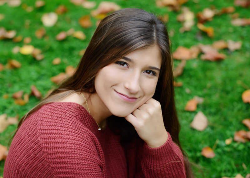 Senior portrait of teen girl in red sweater on grass with fall leaves in Sacramento