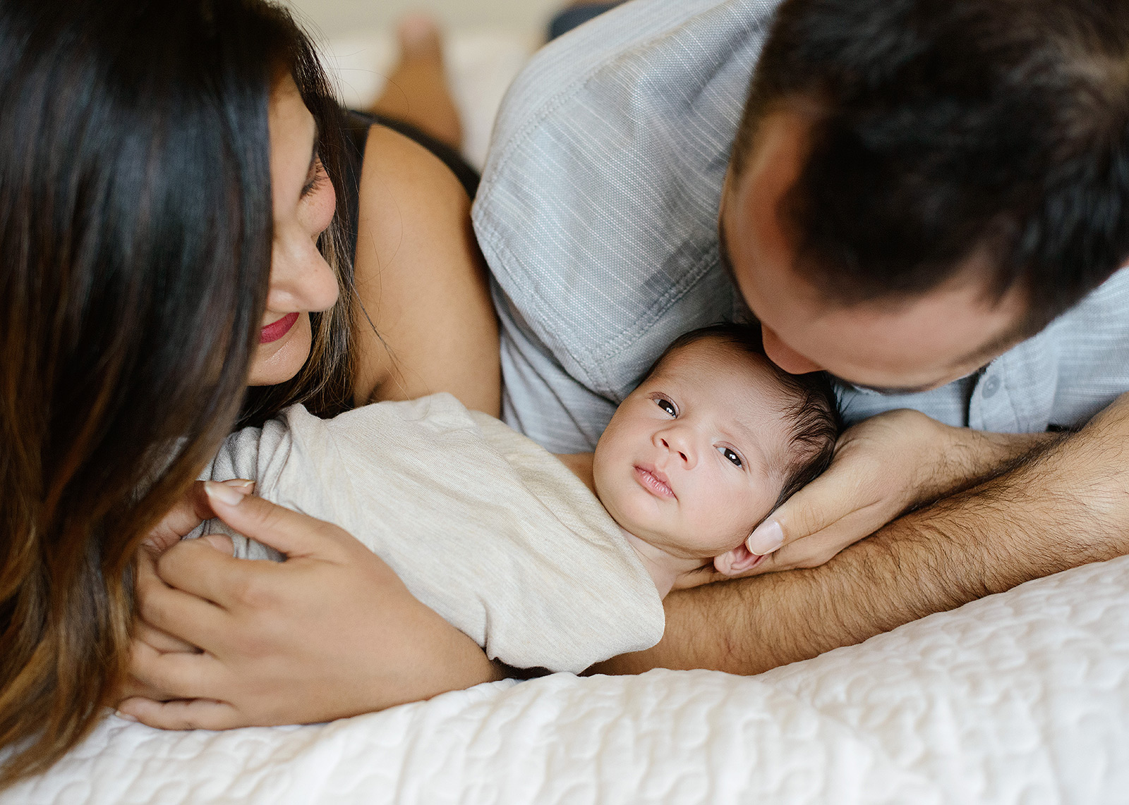 Mom and dad holding baby in bed in West Sacramento lifestyle shoot