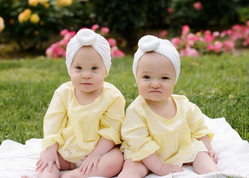 Twin girls wearing yellow and white turban sitting up on grass