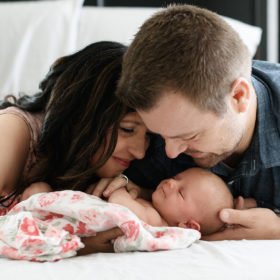 Mom and dad holding newborn baby girl on bed photo shoot in home