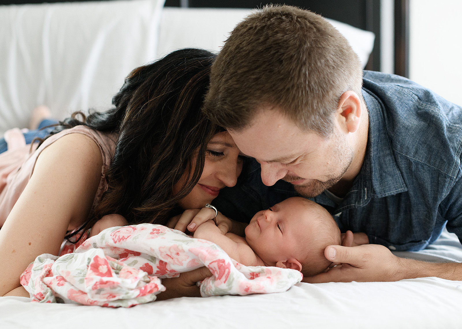 Mom and dad holding newborn baby girl on bed photo shoot in home