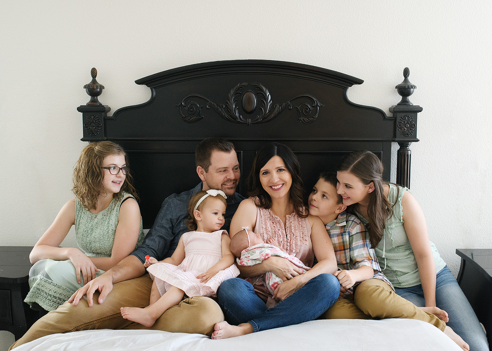 Family photo with newborn baby girl on bed with siblings lovingly looking