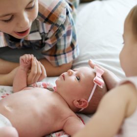 Big brother and big sister hold newborn baby sister on bed lifestyle photo