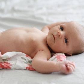 Newborn baby girl on floral swaddle on bed