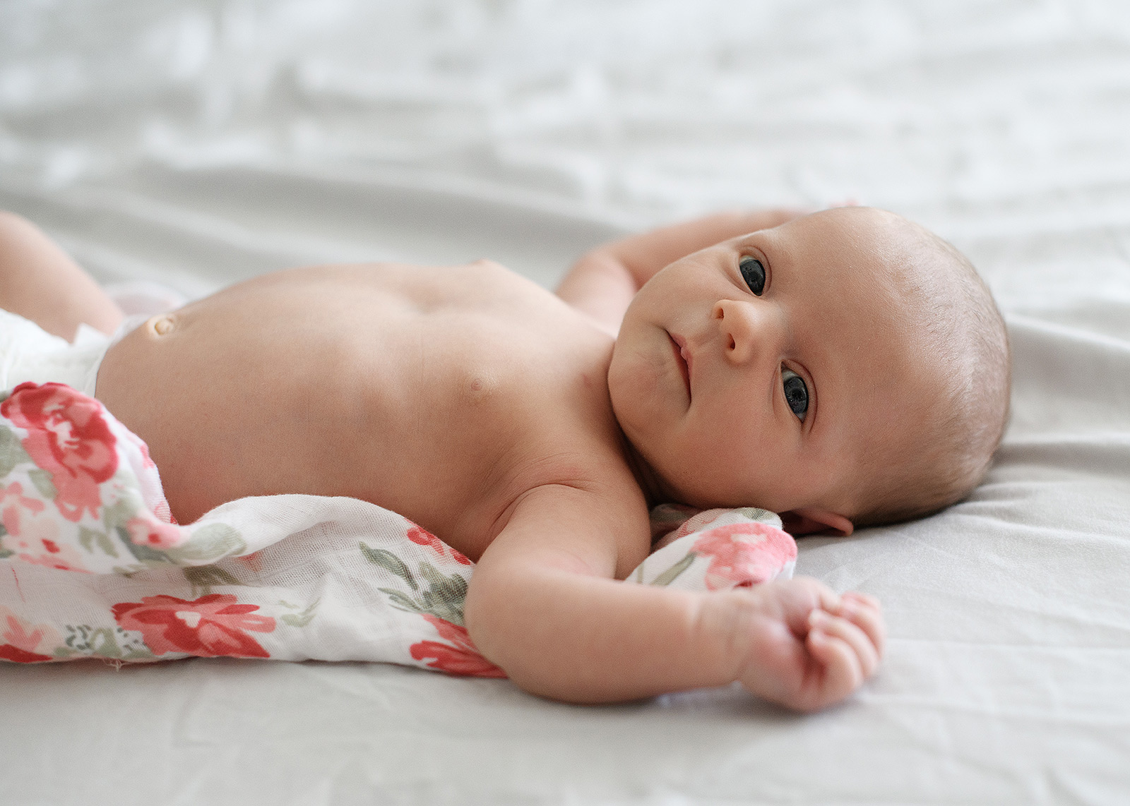 Newborn baby girl on floral swaddle on bed