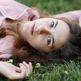 Senior girl lying on grass wearing dusty rose top in Sacramento