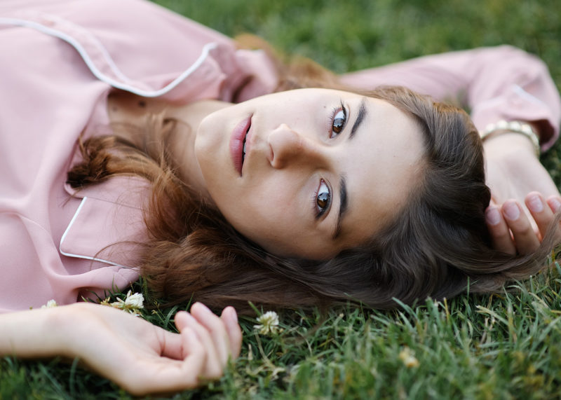 Senior girl lying on grass wearing dusty rose top in Sacramento