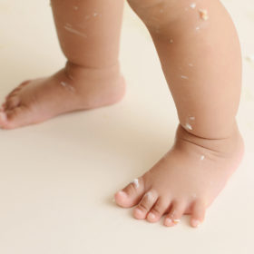 Baby girl’s feet with frosting from cake smash
